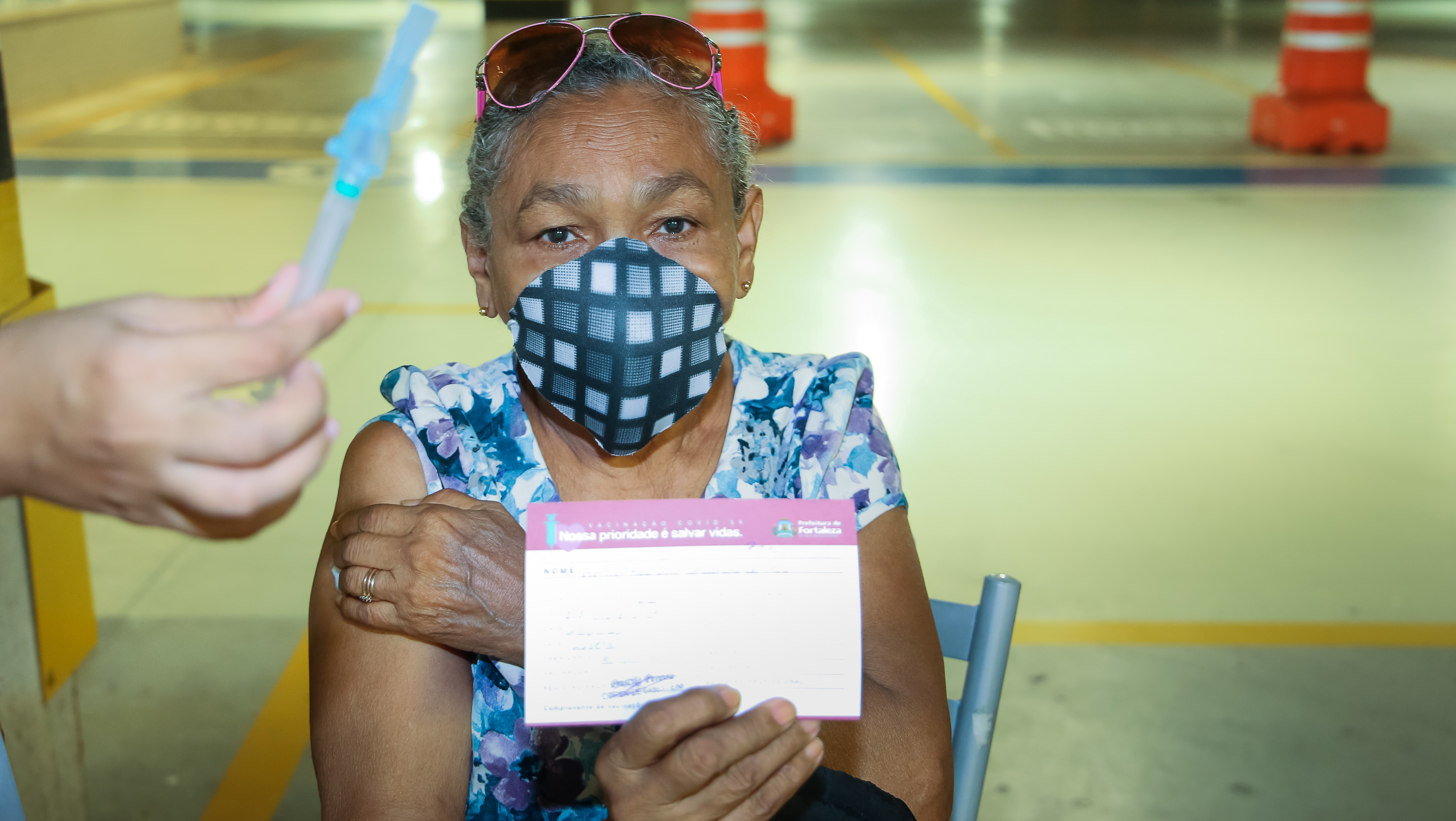 senhora segura cartão de vacinação enquanto olha para a câmera